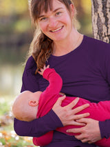 A mother wearing a purple Iksplor merino wool long sleeve nursing top while breastfeeding her baby outdoors. #color_huck-it-berry