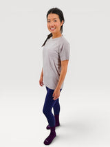 Woman wearing an Iksplor light grey merino wool t-shirt with blue leggings and purple socks in a studio setting #color_trail dust