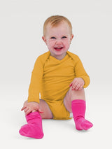 Happy baby wearing a mustard yellow Iksplor merino wool long-sleeve bodysuit and bright pink socks. #color_yellowstone