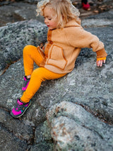 Iksplor kids merino wool base layer leggings in mustard yellow worn by a child sitting on a rocky outdoor surface. #color_yellowstone