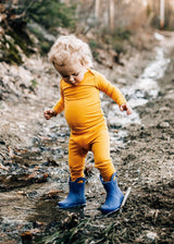 Toddler wearing Iksplor mustard yellow merino wool leggings and long sleeve top while playing in a muddy stream #color_yellowstone