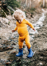 Toddler wearing Iksplor mustard yellow merino wool leggings and long sleeve top while playing in a muddy stream #color_yellowstone