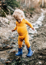 Toddler wearing Iksplor mustard yellow merino wool leggings and long sleeve top while playing in a muddy stream #color_yellowstone