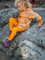 Iksplor kids merino wool base layer leggings in mustard yellow worn by a child sitting on a rocky outdoor surface. #color_yellowstone