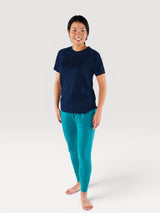 Woman wearing an Iksplor navy blue merino wool t-shirt and teal joggers, standing against a white background. #color_starry night