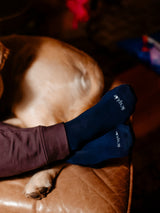 Iksplor navy blue merino wool blend trail socks worn on feet with a dog resting nearby on a leather surface. #color_basecamp