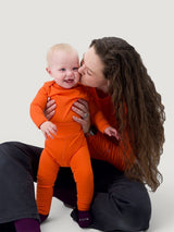Iksplor baby wearing bright orange merino wool leggings with a wide waistband, held by a woman in a matching top. #color_poppy