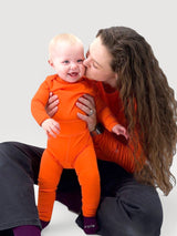 Iksplor baby wearing bright orange merino wool leggings with a wide waistband, held by a woman in a matching top. #color_poppy