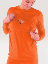 Iksplor bright orange merino wool long sleeve nursing top with discreet chest access and thumb holes on a woman. #color_poppy