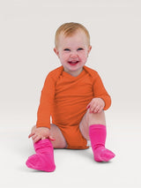 Iksplor baby wearing a bright orange long-sleeve merino wool bodysuit and pink socks, sitting on a white background. #color_poppy