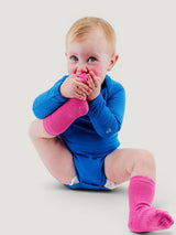 Baby wearing Iksplor bright pink merino wool blend trail socks and a blue long-sleeve bodysuit #color_desert rose