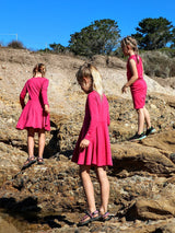 Three girls wearing bright pink Iksplor merino wool adventure dresses while hiking on rocky terrain. #color_peak pink
