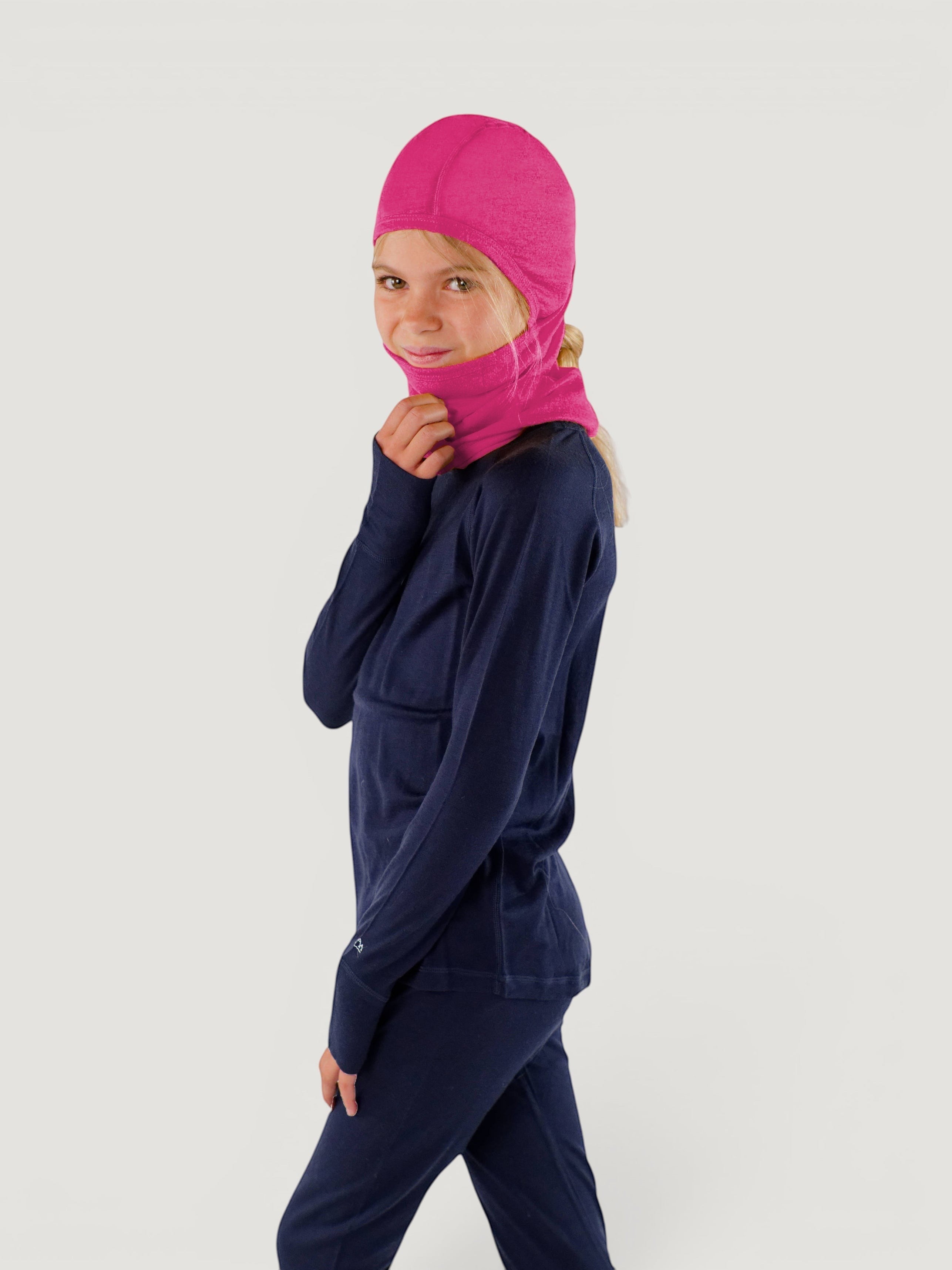 Iksplor pink merino wool balaclava with ponytail hole worn by a young girl in a navy base layer set #color_peak pink