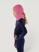 Iksplor pink merino wool balaclava with ponytail hole worn by a child in profile view #color_alpenglow