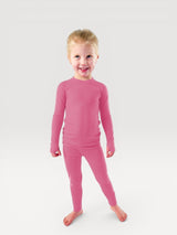 A young child wearing a pink Iksplor merino wool long-sleeve base layer top and matching leggings. #color_alpenglow