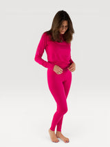 Woman wearing Iksplor bright pink merino wool long sleeve top and matching baselayer leggings on white background #color_peak pink