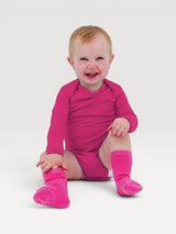 Happy baby wearing a bright pink Iksplor long-sleeve merino wool bodysuit and matching socks #color_peak pink