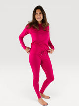 Woman wearing a bright pink Iksplor merino wool long sleeve top and matching leggings against a white background. #color_peak pink