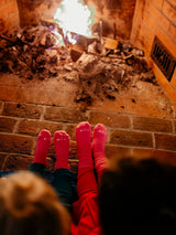Iksplor pink merino wool blend trail socks worn by two people sitting in front of a cozy fireplace. #color_desert rose