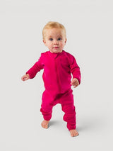 A baby standing in a vibrant pink Iksplor merino wool zip romper with long sleeves and a full-length front zipper. #color_peak pink