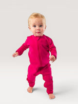 A baby standing in a vibrant pink Iksplor merino wool zip romper with long sleeves and a full-length front zipper. #color_peak pink