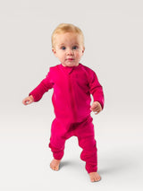 A baby standing in a vibrant pink Iksplor merino wool zip romper with long sleeves and a full-length front zipper. #color_peak pink