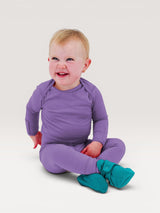 A happy baby wearing a purple Iksplor merino wool long sleeve shirt and matching pants with teal booties. #color_lilac