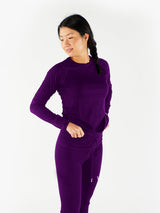 Woman wearing a deep purple Iksplor merino wool long sleeve top with matching leggings against a white background #color_huck-it-berry
