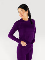 Woman wearing a deep purple Iksplor merino wool long sleeve top with matching leggings against a white background #color_huck-it-berry