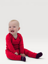 Happy baby wearing Iksplor red merino wool leggings with a comfortable wide waistband, sitting on a white background. #color_campfire