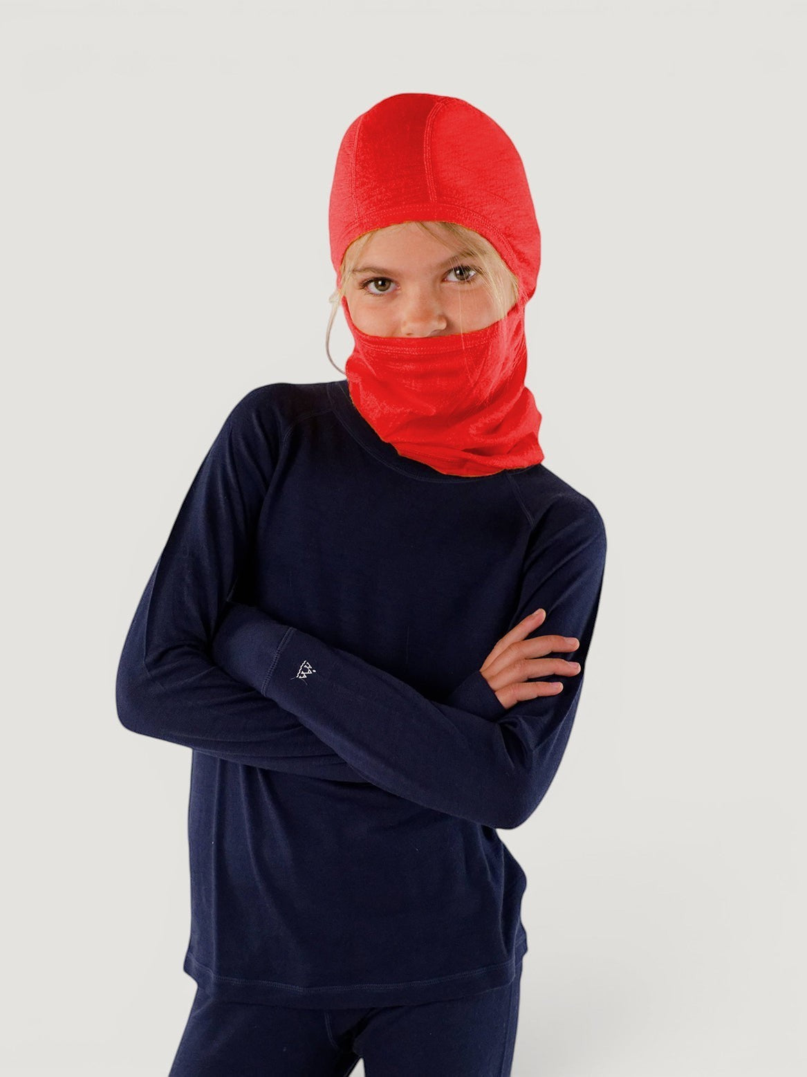 Child wearing a bright red Iksplor merino wool balaclava with a ponytail hole and a navy long-sleeve base layer. #color_campfire