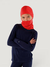 Child wearing a bright red Iksplor merino wool balaclava with a ponytail hole and a navy long-sleeve base layer. #color_campfire