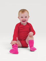 Iksplor baby merino wool long-sleeve bodysuit in bright red worn by a smiling toddler with pink socks #color_campfire