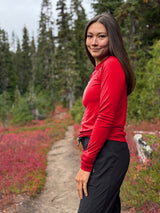Woman wearing a red Iksplor merino wool long sleeve top while hiking on a forest trail #color_campfire