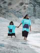 Iksplor x SURreal turquoise and dark brown terry cloth towel poncho worn by a mother and child on a beach. #color_high tide