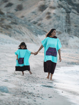 Iksplor x SURreal turquoise and dark brown terry cloth towel poncho worn by a mother and child on a beach. #color_high tide