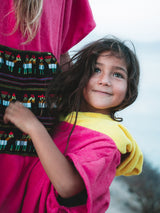 Iksplor x SURreal pink and yellow terry cloth towel poncho worn by a smiling child outdoors #color_wild fuchsia
