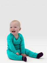 Happy baby wearing bright teal Iksplor merino wool leggings and matching long sleeve shirt against a white background #color_tidepool