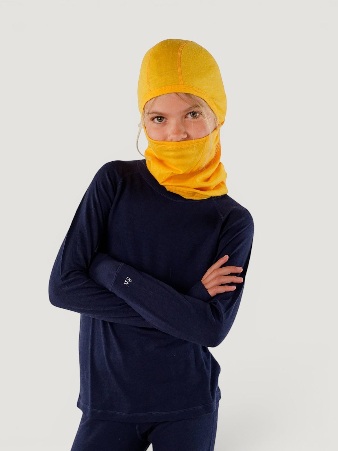 Child wearing a bright yellow Iksplor merino wool balaclava with a ponytail hole and a navy long-sleeve base layer. #color_yellowstone